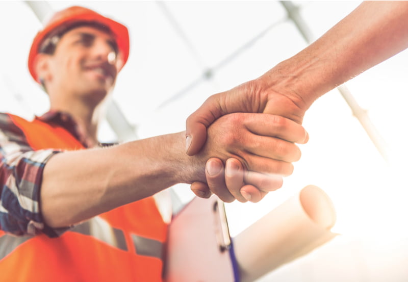 Construction workers in protective helmets and vests are shaking hands