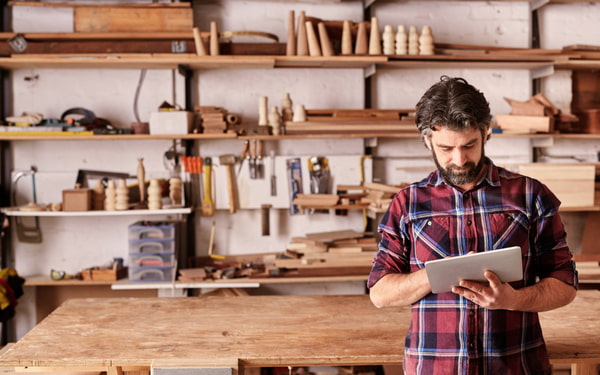 Carpenter standing in his workshop using a digital tablet
